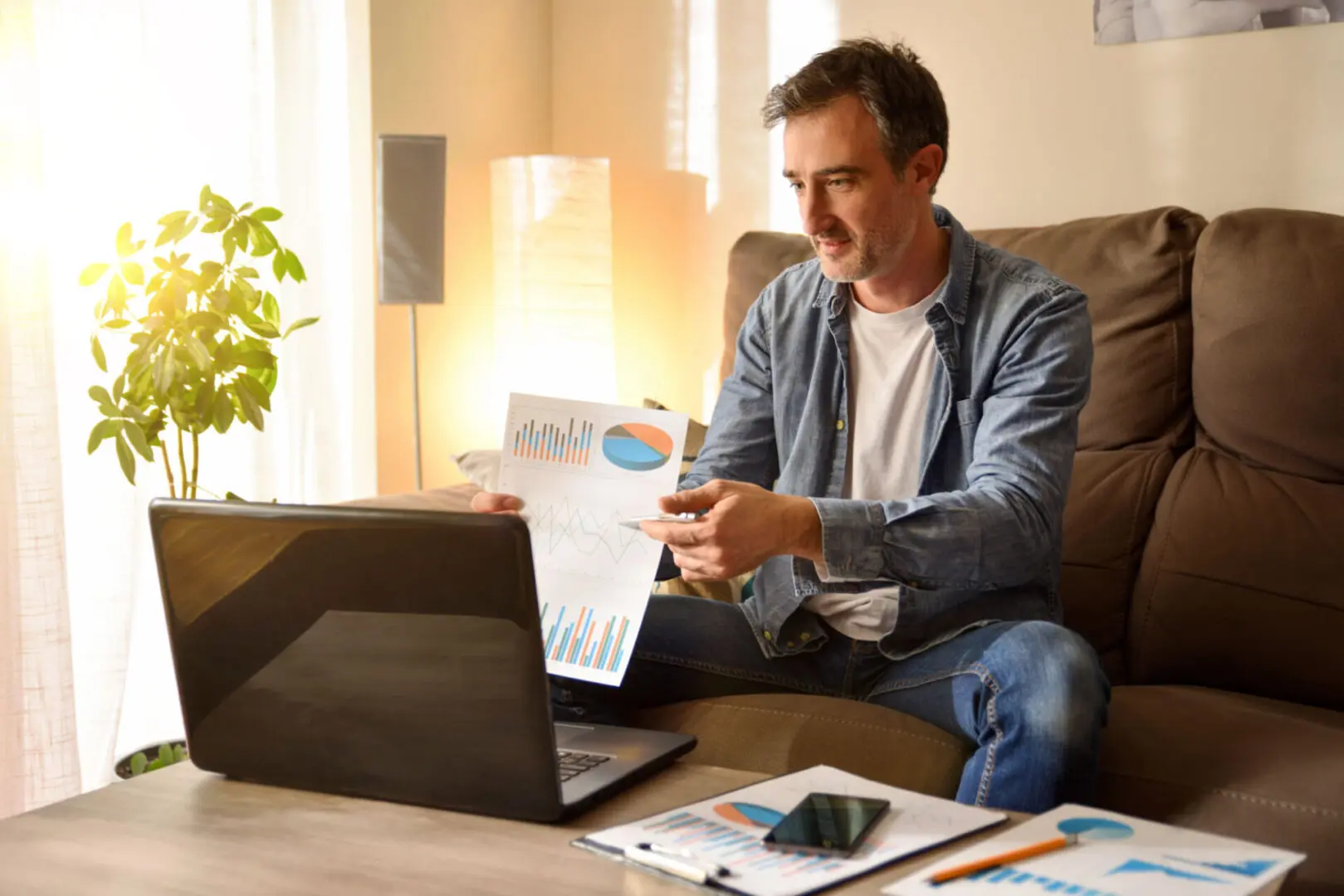Man analyzing charts on laptop at home.