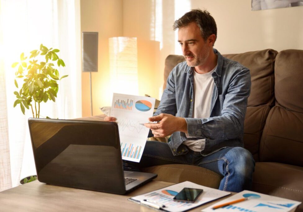 Man analyzing charts on laptop at home.